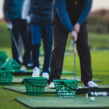 Group of golfers practicing and training golf swing on driving range practice, men playing on golf course, golf ball at golfing complex club resort, summer sunny day