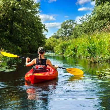 Girl with paddle and kayak on a small river in rural landscape