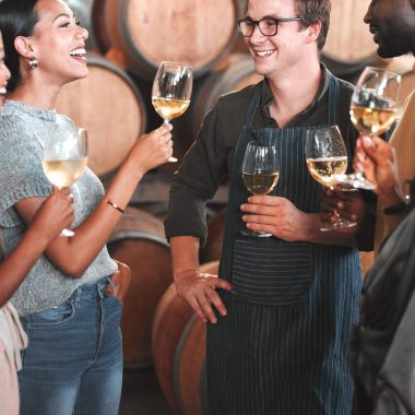 Group of friends wine tasting at a distillery or cellar drinking glasses and enjoying the tour together. Happy, carefree and diverse people bonding and having fun at a winery estate.